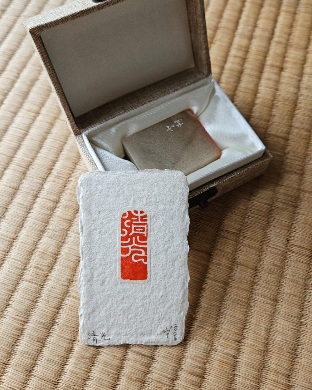 Detail of a carved square seal beside a taller stone, on handmade paper