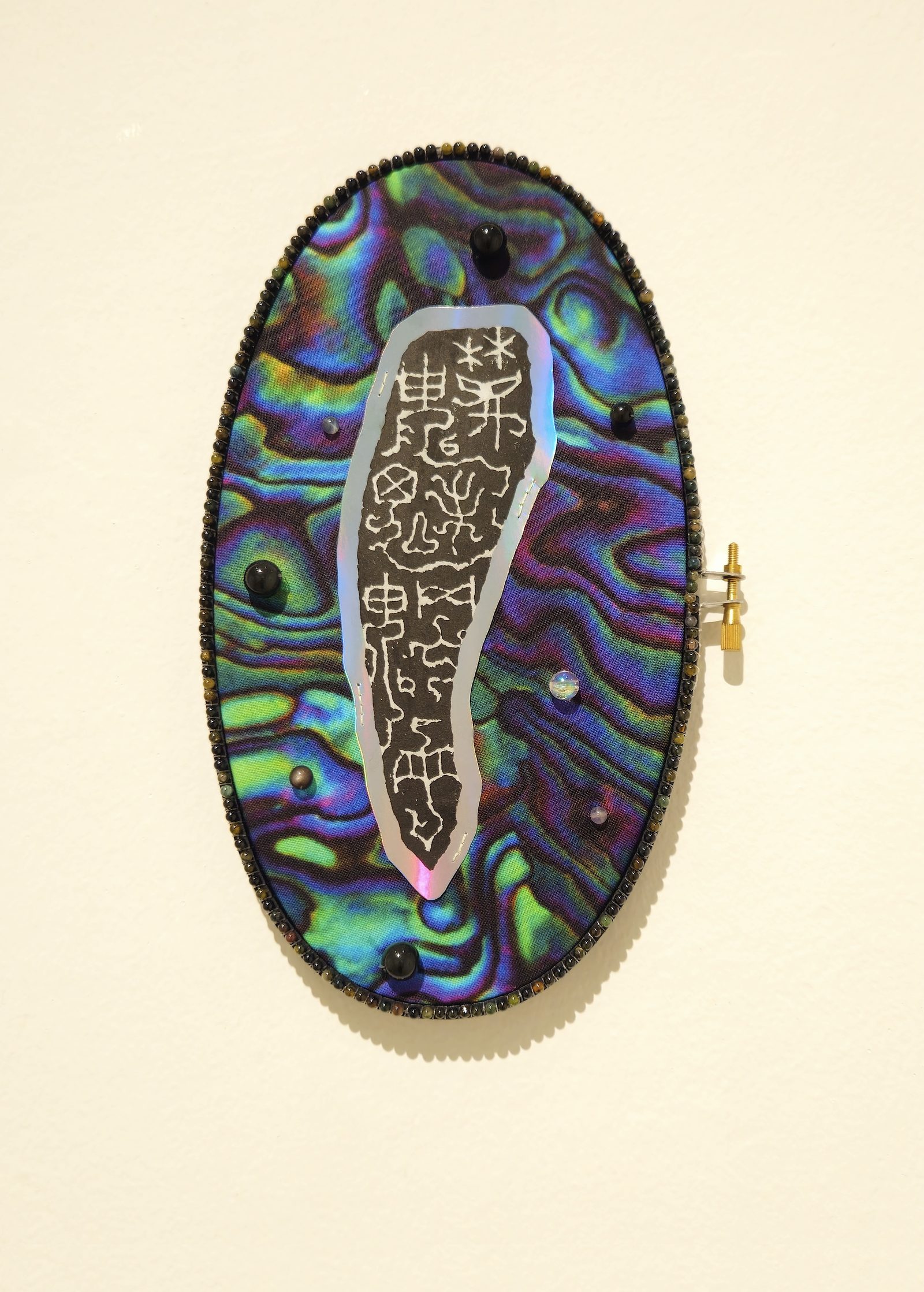 Iridescent oval piece with carved seal and beaded border