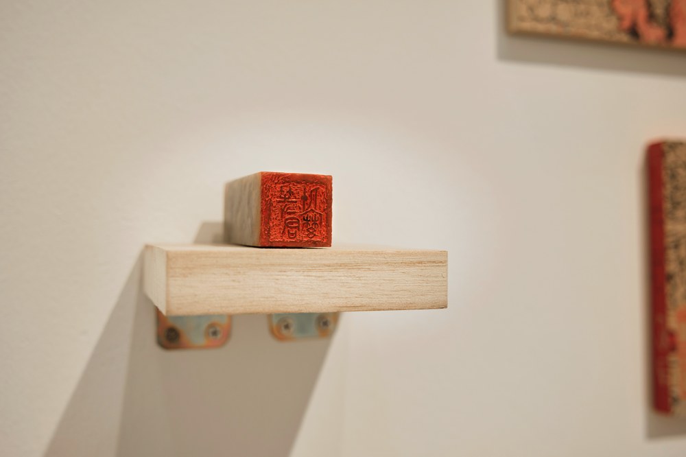 Red cube seal on wooden shelf — detail