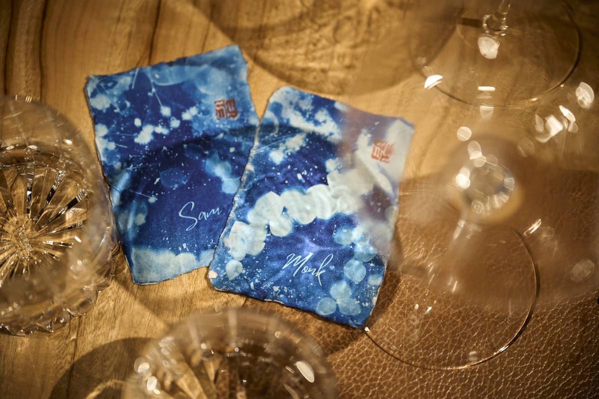 Two cyanotype wedding place cards with red seal stamps, among crystal glasses
